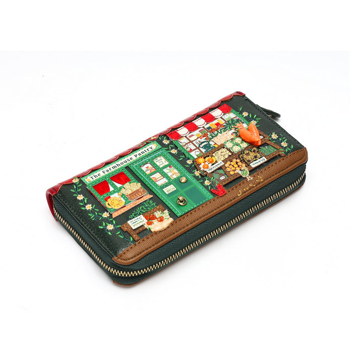 A zip-around wallet featuring a detailed miniature street market scene on the front, with green storefronts, red-and-white awnings, small decorative figures, and a gold zipper.