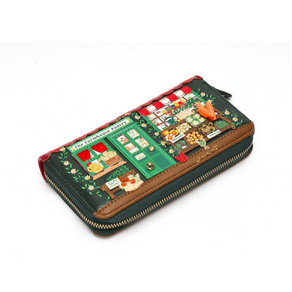 A zip-around wallet featuring a detailed miniature street market scene on the front, with green storefronts, red-and-white awnings, small decorative figures, and a gold zipper.