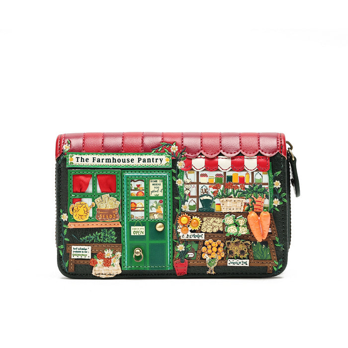 A rectangular zip-around clutch purse featuring a detailed patchwork illustration of a vintage grocery store storefront labeled 'The Farmhouse Pantry.' The design includes a red quilted top border, green door and window panels, black background sections, and colorful embroidered-style vegetable and fruit motifs such as carrots, flowers, and produce.