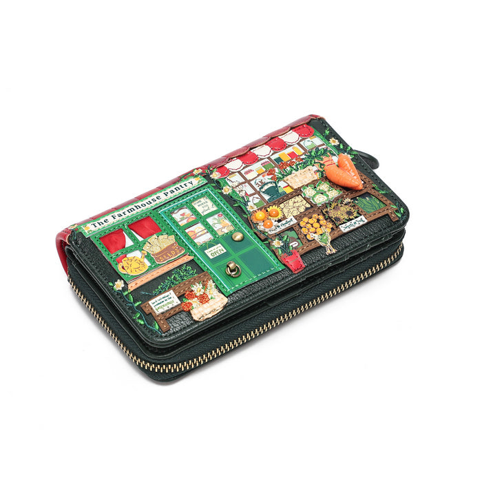 A black zip-around wallet with a highly detailed, colorful cartoon-style illustration on the front depicting a farm market scene, complete with a carrot character and small text reading 'The Farmhouse Farm'.