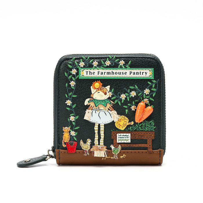 A small zip-around wallet with a dark green textured exterior and a brown base, decorated with a whimsical illustration of a girl in a white dress standing in a garden with flowers, carrots, and small animals. A sign reads 'The Farmhouse Pantry'.