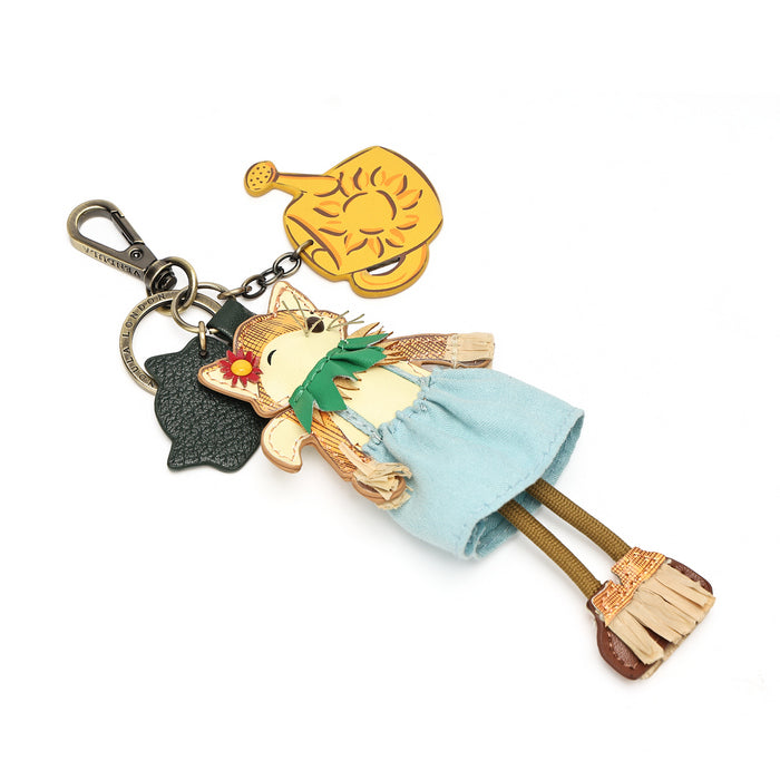 A Hawaiian-themed keychain featuring a Catwoman character dressed in a light blue skirt, green lei, and brown hair, holding a gold pineapple, attached to a silver clasp with a black tag.