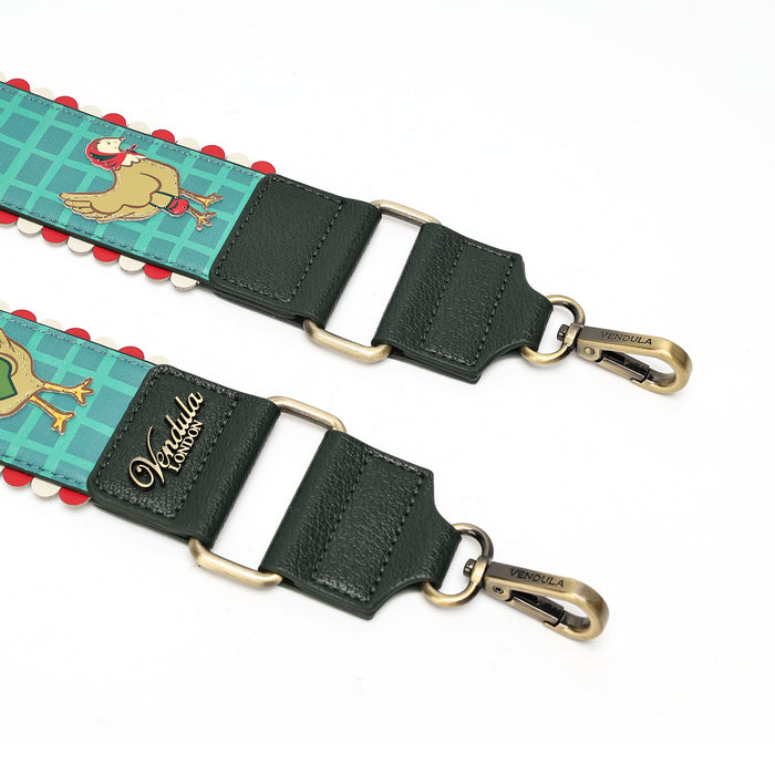 A close-up of a shoulder strap featuring dark green leather sections, antique brass hardware, and a turquoise blue patterned fabric with a cartoon camel illustration and red and white pom-pom trim.