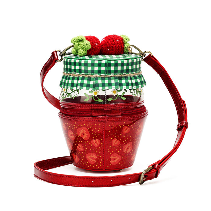A strawberry-themed bucket bag with a red glossy body, a green and white gingham checkered lid, a clear upper section with floral details, and two crocheted red strawberries on top, shown on a white background.