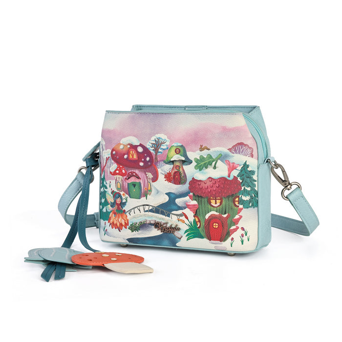 A square-shaped light blue crossbody handbag featuring a whimsical winter forest illustration with mushroom houses, a snowy bridge, and a small treehouse. The bag has a matching light blue strap and silver-tone hardware, with decorative tag accents hanging from the side.