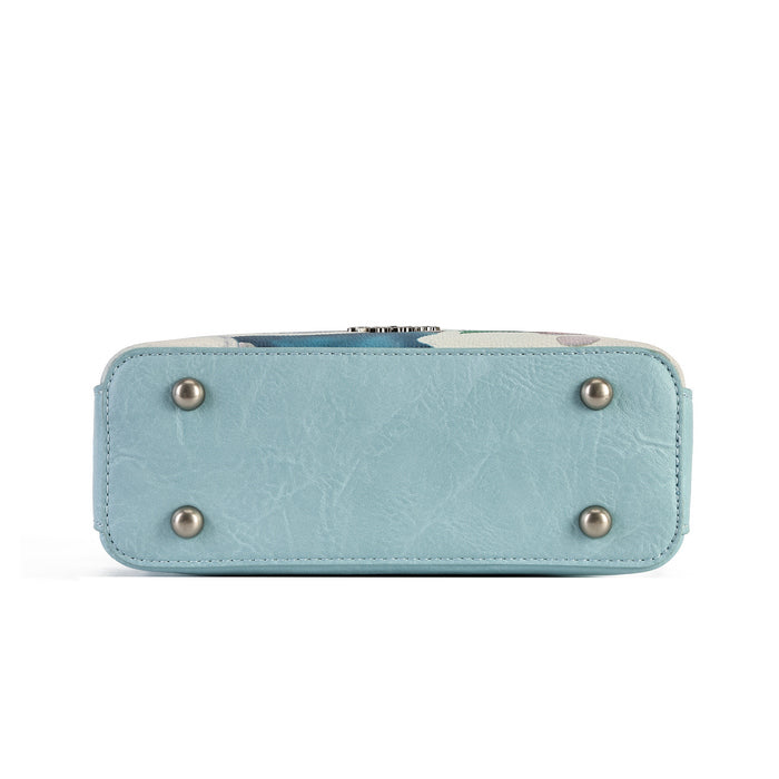 A square-shaped light blue crossbody handbag featuring a whimsical winter forest illustration with mushroom houses, a snowy bridge, and a small treehouse. The bag has a matching light blue strap and silver-tone hardware, with decorative tag accents hanging from the side.