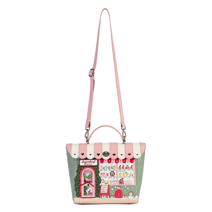 A pastel pink and sage green handbag with a whimsical storefront illustration on the front, featuring a pink shoulder strap, top handle, and silver-tone hardware on a plain white background.