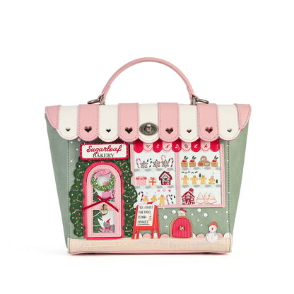 A structured handbag with a pink and cream striped top handle and flap, featuring a detailed Christmas bakery storefront applique on the front with green, red, pink, and white elements.