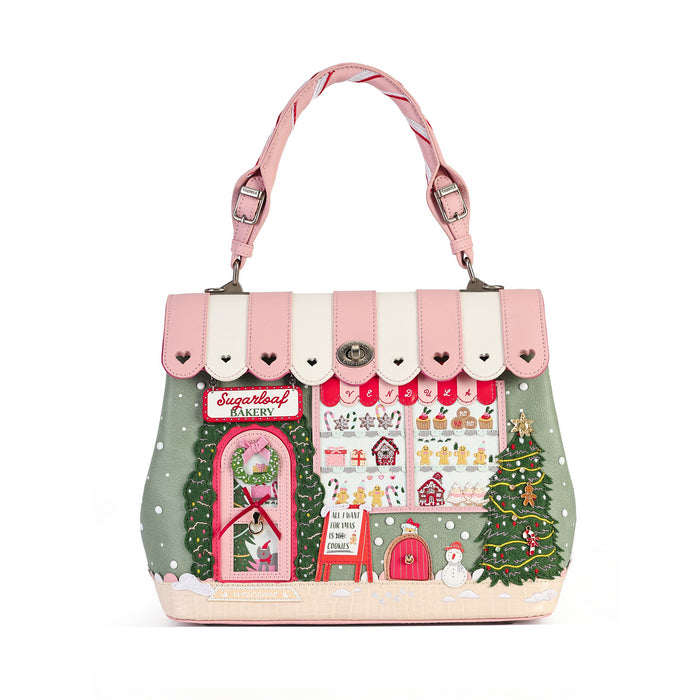 A handbag designed to look like a festive Christmas bakery storefront, featuring pink and cream striped awning, a pink handle, and a detailed winter scene printed on the front with a bakery window, Christmas tree, and snow.