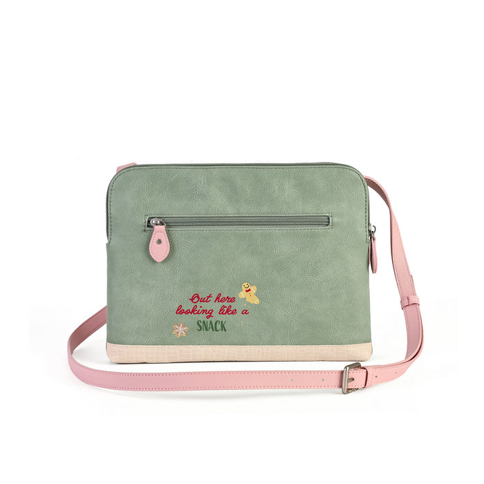 A sage green crossbody laptop bag with a pink strap and zipper pull, featuring a front zip pocket with a pink tab and embroidered text reading 'But here looking like a snack' with a small dog illustration.