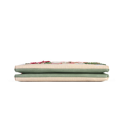 A folded fabric cushion or pad with a sage green top and cream-colored sides, featuring a small embroidered floral detail on the upper edge, set against a plain white background.