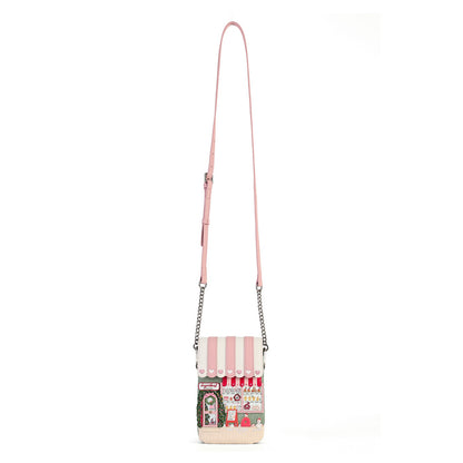 A pink faux-leather crossbody bag with a long shoulder strap and silver chain links, featuring a whimsical storefront graphic on the front pocket with strawberries, a cat, and the text 'Café Strawberry'.