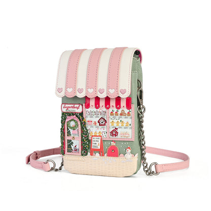A whimsical, multi-material crossbody phone bag with a pink and cream striped awning, a detailed storefront patchwork design, and a pink strap with silver chain links, shown on a white background.