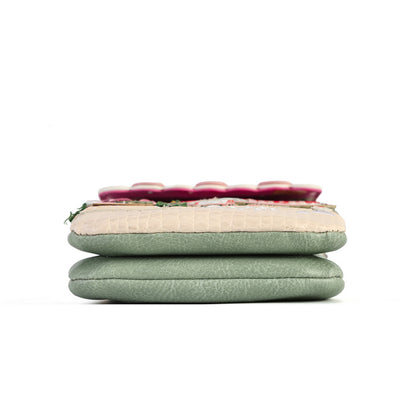 A folded green faux-leather clutch or wallet with a beige crocodile-embossed panel and a row of red flower appliqués, stacked on a white background.