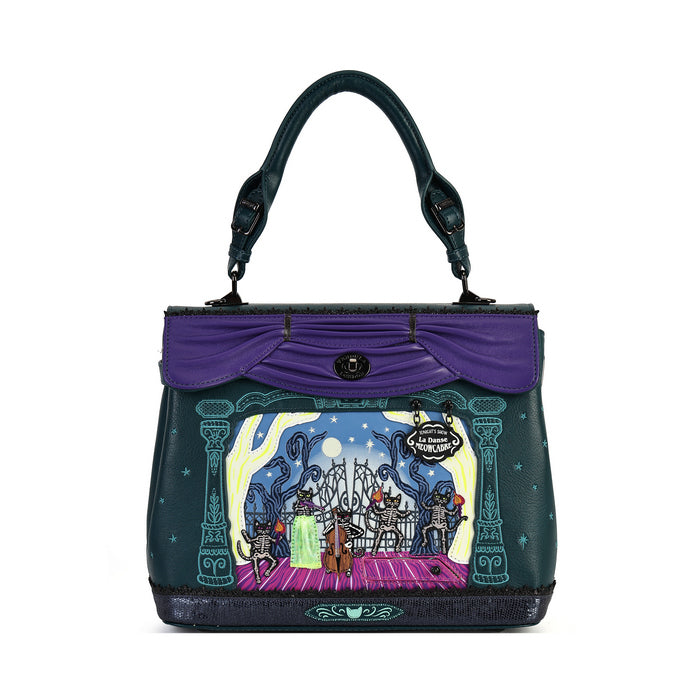 A dark teal handbag with a purple top flap and handle, featuring a colorful illustrated scene of a fairground or stage on the front panel.