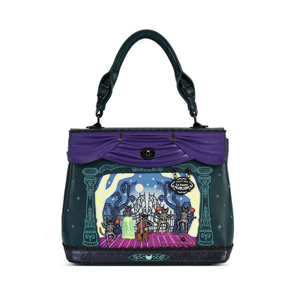 A dark teal handbag with a purple top flap and handle, featuring a colorful illustrated scene of a fairground or stage on the front panel.