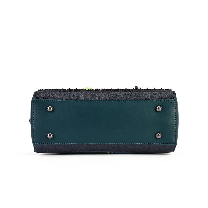 The bottom view of a dark teal leather clutch bag with a black woven trim along the zipper and silver-tone metal studs on the base, shown against a plain white background.