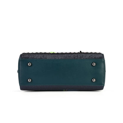 The bottom view of a dark teal leather clutch bag with a black woven trim along the zipper and silver-tone metal studs on the base, shown against a plain white background.