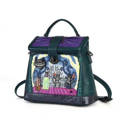 A dark teal and purple handbag with a whimsical illustrated front panel showing skeleton characters on a stage. The bag has a top handle, a front flap with a purple interior lining, and a detachable shoulder strap, photographed on a clean white background.