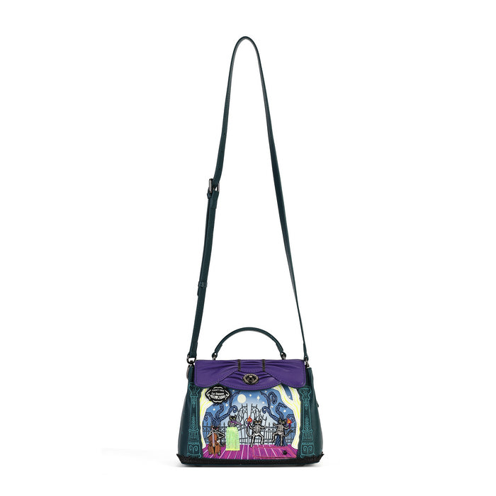 A structured handbag with a purple top handle and a colorful illustrated front panel, featuring a dark green shoulder strap and side fringe, photographed on a plain white background.