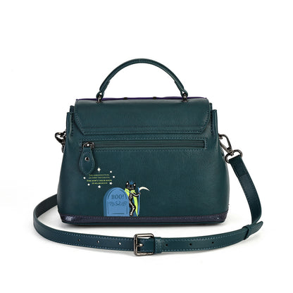 A dark teal leather handbag with a top handle, front zip pocket, and an attached shoulder strap, featuring a small cartoon tombstone graphic on the front.