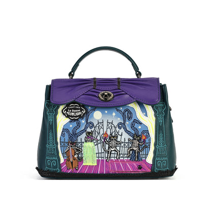 A purple and dark teal handbag with a top handle, featuring a decorative front panel illustration of a nighttime scene with skeletons, a cello, and the text 'La Danse des Mortels'.