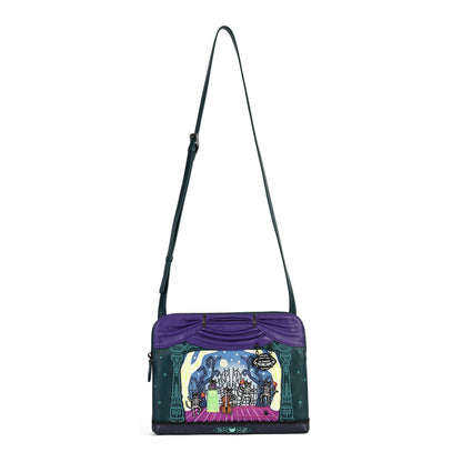 A purple and dark green crossbody bag featuring a colorful, whimsical fantasy illustration on the front depicting a castle and a character holding a green gift. The bag has a long dark green strap and a small hanging charm.