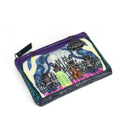 A small zippered pouch with a purple zipper and a colorful printed design featuring skeletons, a gate, a green coffin, and swirling blue and yellow patterns. A black hangtag is attached near the top right corner.