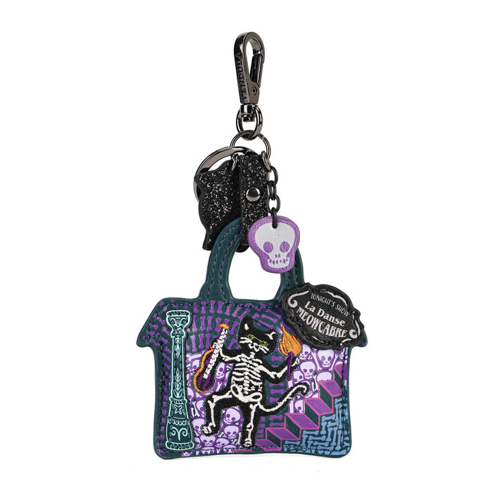 A decorative keychain shaped like a small handbag with a skeleton dancing on purple steps, attached to a black carabiner and key rings. The bag has a dark teal body, purple and black patterned details, a black skull charm, and a black hanging tag reading 'La Danse des Médicaux'.