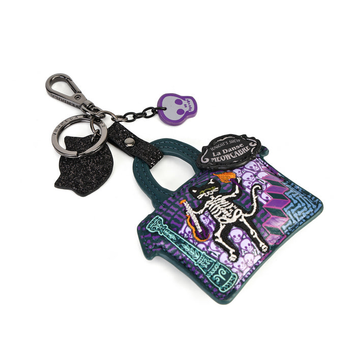 A Halloween-themed keychain shaped like a small purse, featuring a purple and teal patterned body with a skeleton graphic, a black cat silhouette charm, a small purple skull tag, and a silver clasp on a white background.