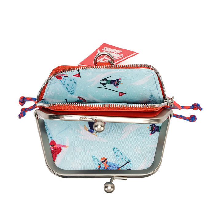 A small coin purse with a light blue winter sports print featuring skiers and snow, framed in silver-tone metal with a red zipper and red-and-blue braided zipper pulls. A red hangtag is attached at the top, photographed on a plain white background.
