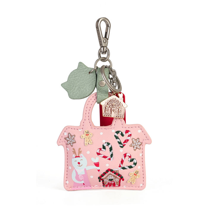 A pink faux-leather handbag-shaped Christmas keychain or bag charm with a silver clasp, featuring a green leaf tag, a red ribbon, a gingerbread house charm, and festive appliques including candy canes, a reindeer, and snowflakes on a white background.