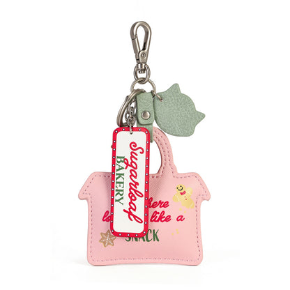 A pink handbag-shaped keychain or bag charm with a silver clasp, a mint green cat-shaped tag, and a hanging tag that reads 'Superfood BAKERY'. The pink body features the text 'There is one like a SNACK' and a small yellow cartoon character.