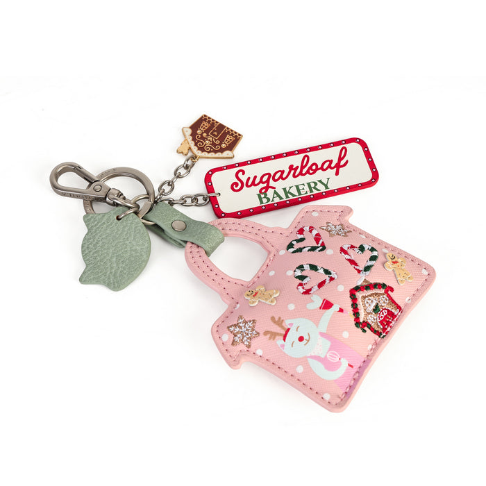 A pink Christmas-themed handbag-shaped keychain bag with a silver clasp, a green leaf charm, a brown bakery tag charm, and a red-and-white 'Sugarloaf Bakery' label. The bag features holiday illustrations including a snowman, gingerbread house, candy canes, and stars on a white background.