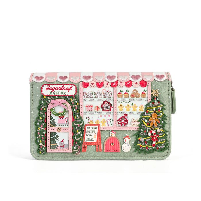 A mint green zip-around wallet featuring a detailed Christmas market scene design on the front, complete with a bakery storefront, decorated Christmas trees, a pink awning with hearts, and small embroidered details.