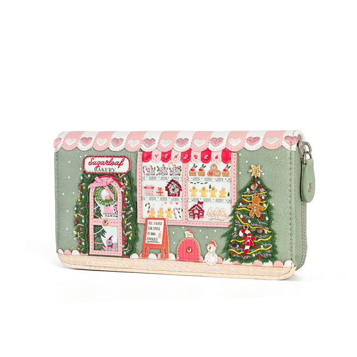 A mint green zip-around wallet featuring a detailed Christmas storefront illustration with a pink scalloped awning, candy shop window, decorated tree, gingerbread man, and snowman, shown on a white background.