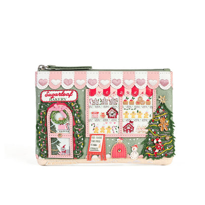 A zip-around clutch purse featuring a detailed Christmas bakery storefront design with pink and white striped awning, decorated windows, a green wreath, a Christmas tree, and a snowman, shown on a plain white background.