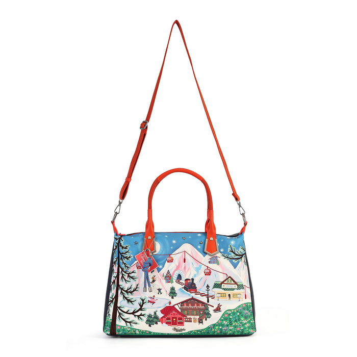 A structured tote bag with a vibrant winter mountain village illustration on the front, featuring red leather handles and a red shoulder strap, set against a plain white background.