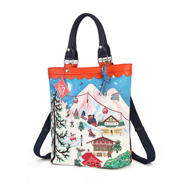 A tote bag with a colorful winter mountain village illustration on the front, featuring a bright orange-red scalloped top trim, black handles, and a black shoulder strap, shown on a plain white background.