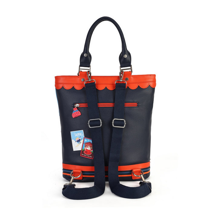 A navy blue leather tote bag with bright orange trim, scalloped orange top edge, and matching orange horizontal accents. It features dual top handles, a detachable shoulder strap, and two decorative travel stickers attached to the front pocket, set against a plain white background.