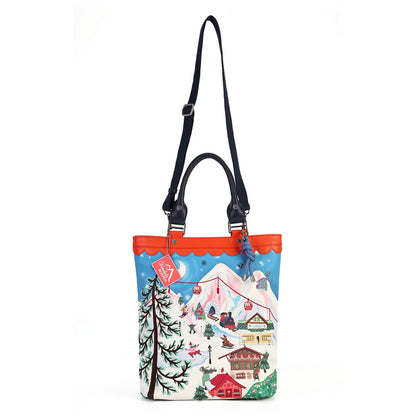 A tote bag with a colorful winter mountain scene printed on the front, featuring a bright orange-red scalloped trim, black shoulder straps, and a blue sky background in the illustration.