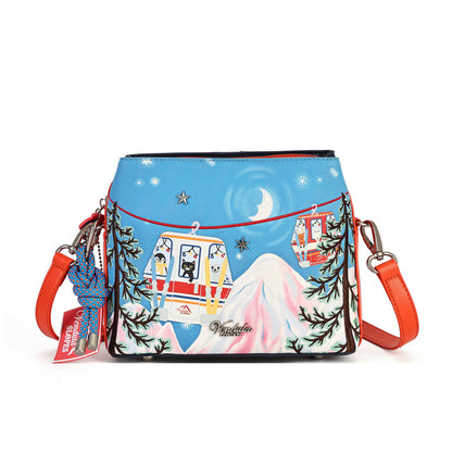 A small crossbody bag with a bright blue winter mountain scene printed on the front, featuring cable cars, stars, evergreen trees, and a red-orange strap. A hanging tag on the left reads 'Winter Wonderland' and includes a blue beaded charm.
