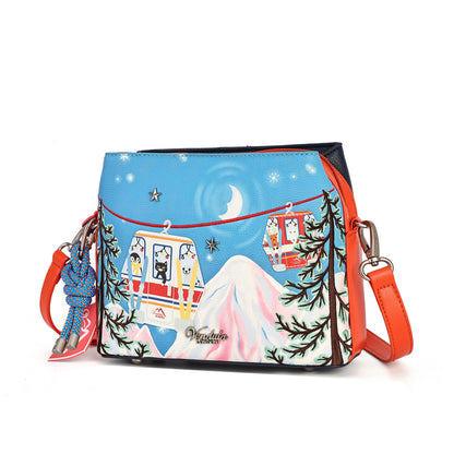 A square-shaped crossbody bag featuring a colorful winter cable car illustration on a light blue background, with a pink mountain, evergreen trees, stars, and a crescent moon. The bag has orange-red trim and straps, a blue braided charm, and a small metal plaque reading 'Vesuvius Design'.