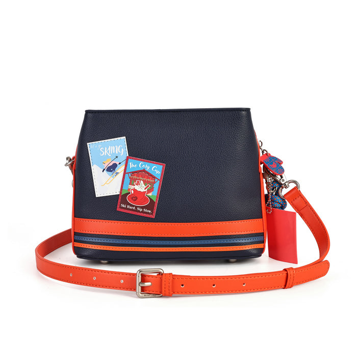 A navy blue pebbled leather crossbody bag with a bright orange leather trim and strap, featuring decorative book-themed stickers and a red tag, shown on a white background.