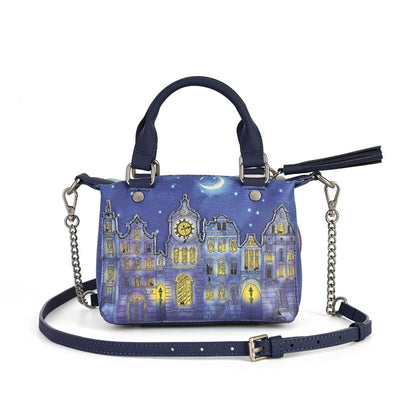 A navy blue handbag featuring a printed illustration of a whimsical village at night under a crescent moon, with silver-tone chain shoulder straps and a matching navy blue top handle.