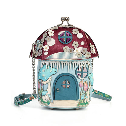 A whimsical, fairy-tale-inspired house-shaped handbag with a mushroom cap roof, blue door, and floral details, shown on a plain white background.