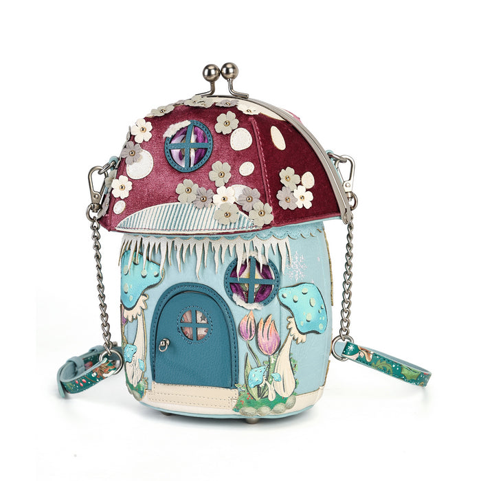 A whimsical fairy-tale house shaped crossbody bag with a burgundy mushroom cap, white cherry blossoms, a blue door, and pastel floral details, shown on a white background.