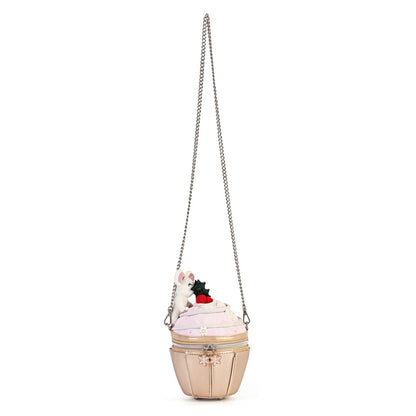 A whimsical cupcake-shaped shoulder bag in pale pink and beige, featuring a silver chain strap, a small white bunny, and a red strawberry decoration on top, set against a plain white background.