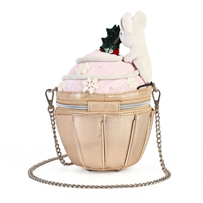 A cupcake-shaped shoulder bag with a metallic champagne-gold body, a light pink frosting top, white snowflake decorations, a plush white bunny on the side, and a small holly sprig on top. It has a silver chain strap and is photographed on a solid white background.