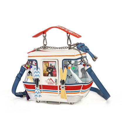 A white faux-leather shoulder bag designed to look like a small boat, featuring a clear front window, blue straps, a red top handle, and various colorful decorative elements including a penguin plush, yellow knit scarf, and multicolored beads.